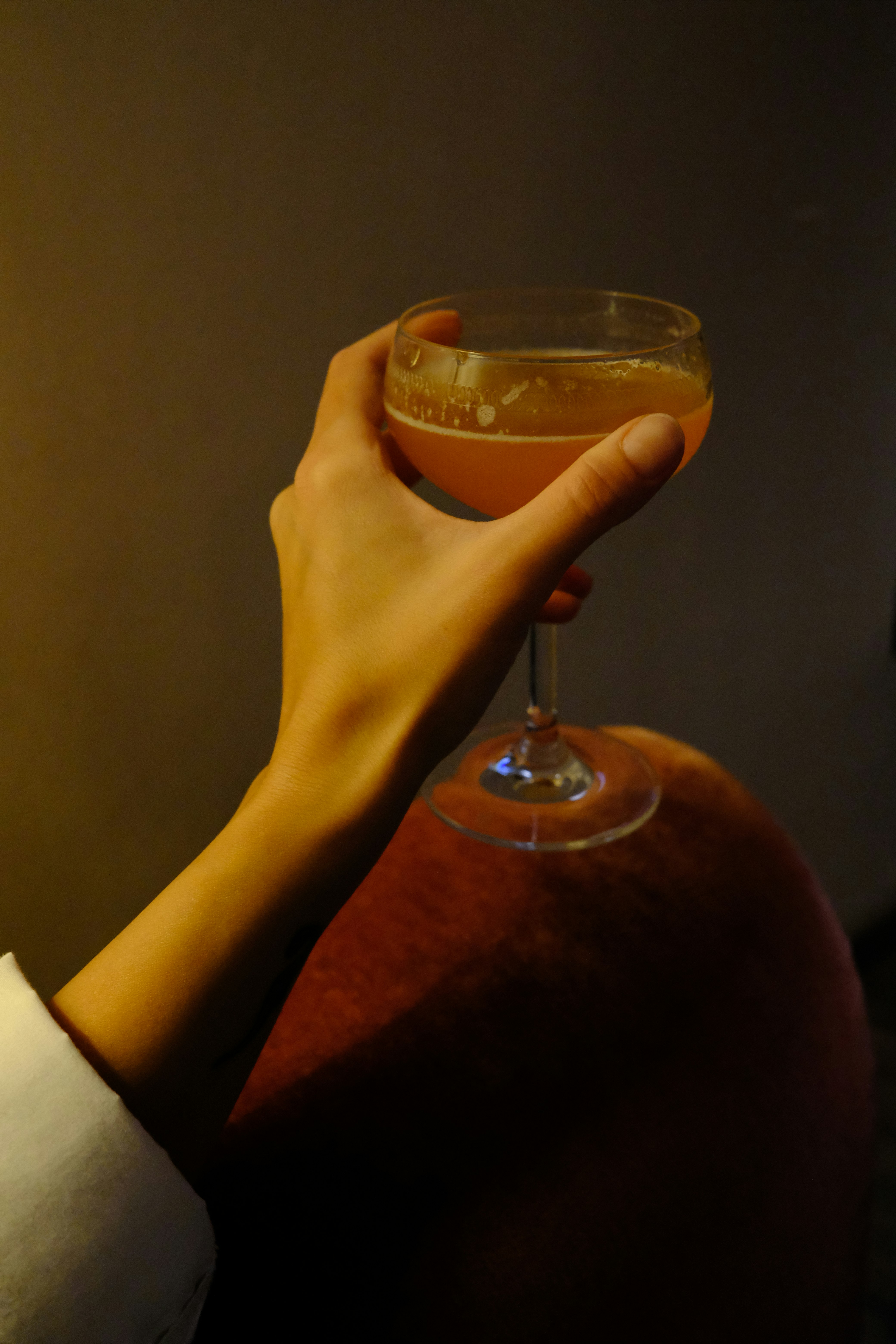 person holding clear wine glass with brown liquid
